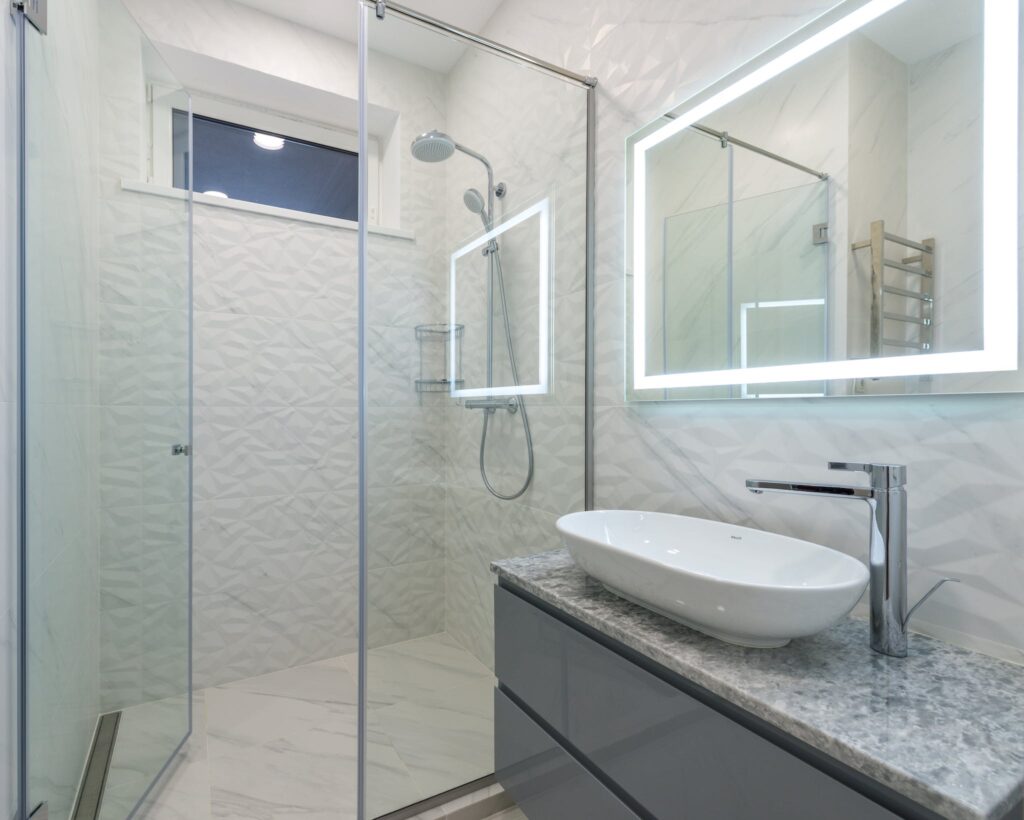Stylish mirror illumination shining in bathroom above sink with faucet and shower cabin